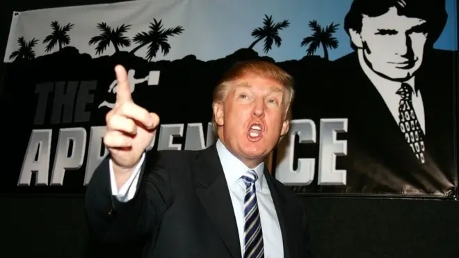 Дональд Трамп на фоне плаката The Apprentice
