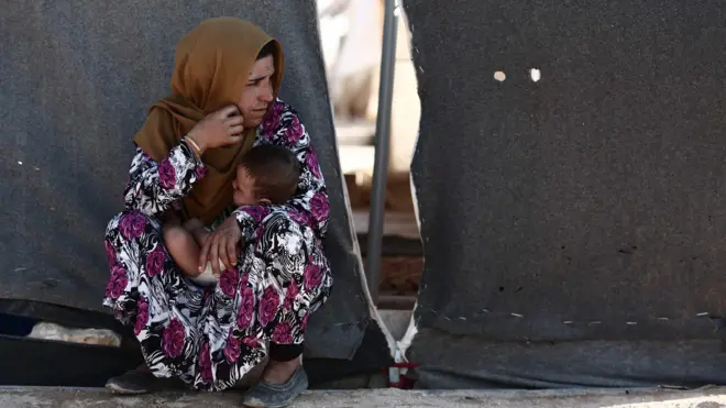 A woman carries her child as she sits in front of a tent at a camp for displaced people in al-Ghadfa, Idlib province, Syria (2 September 2018)