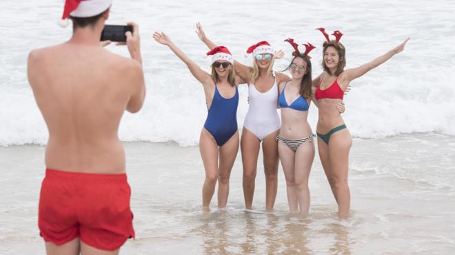 澳大利亞悉尼邦代海灘上一名青年給幾位戴上聖誕帽、身穿泳衣的女士拍照（25/12/2017）