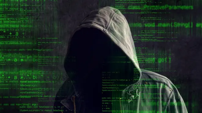 Una persona con una capucha, contra un fondo de códigos de computación.