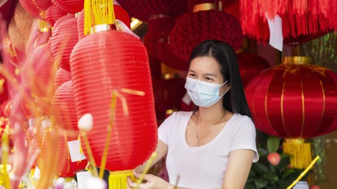 Attractive Woman wearing facemask choosing lantern in a market place, preparing to decorate the house during Chinese New Year