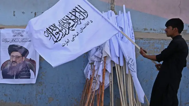 A vendor holds a Taliban flag next to a poster of Taliban leader Abdul Ghani Baradar as he waits for customers along a street in Kabul on August 27, 2021.