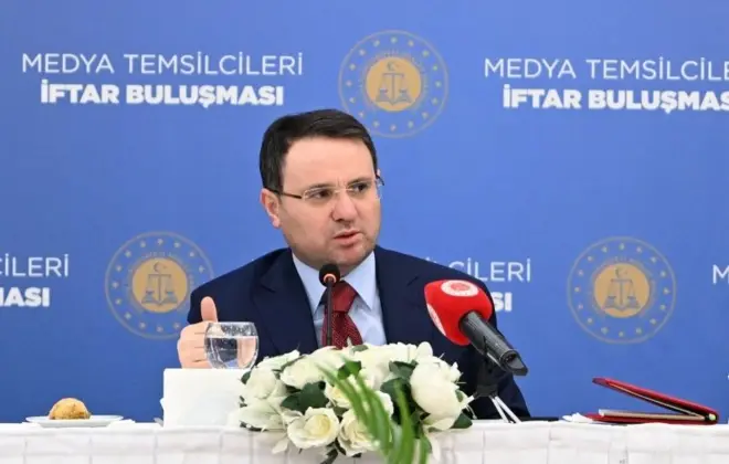 Akın Gürlek ardında medya temsilcileri iftar buluşması yazılı mavi bir panonun önünde oturuyor. Önünde çiçek ve mikrofon var. 