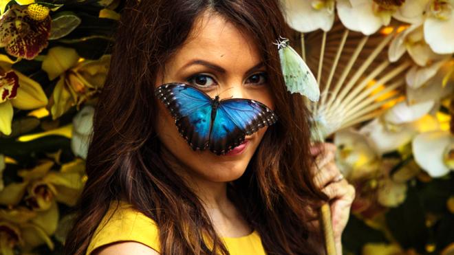 A Blue Morpho butterfly sits on the face of model Jessie Baker