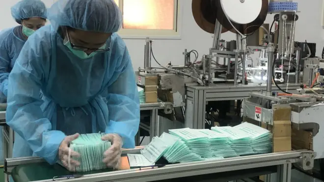 台灣口罩工廠的作業員將機台上的口罩放到盒子內排好、裝箱。