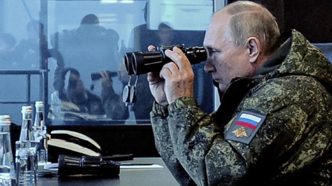 Vladimir Putin vestido con uniforme militar y mirando a través de un largavistas.