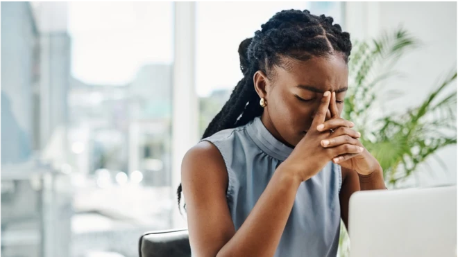 Femme noire stressée travaillant sur un ordinateur portable dans un bureau, seule.
