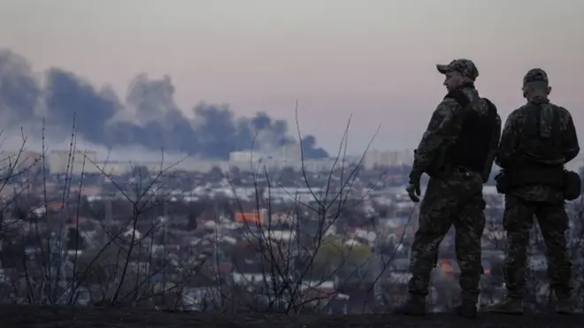 Ukrainian soldiers look at a column of smoke that rises from the Kulinichi bread factory after it was hit by shelling in Kharkiv