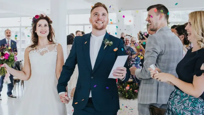Married couple walk down the aisle as colourful confetti is thrown