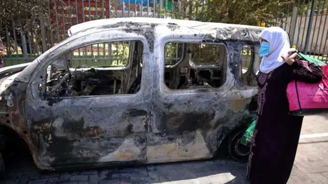 Una mujer pasa frente a un vehículo incendiado en Lod.