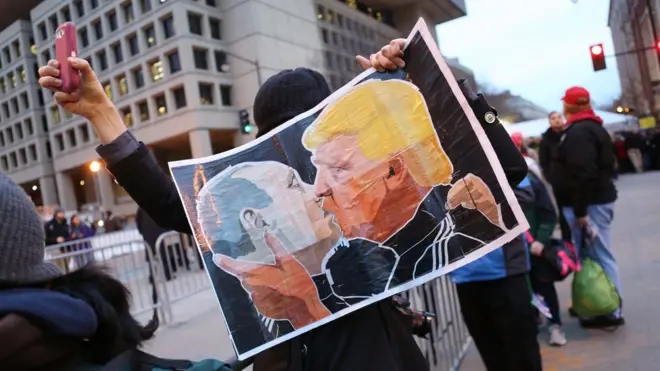 Протестувальник із плакатом з обличчями Трампа і Путіна