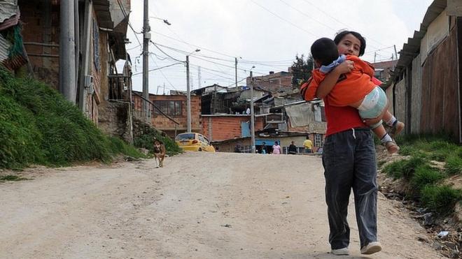 Un niño carga en brazos a otro niño en un barrio de Bogotá.