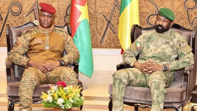 Burkina Faso president on di left wearing military uniform and red beret, Mali president sit for di right hand side wearing military uniform and green beret. Flags dey dia back