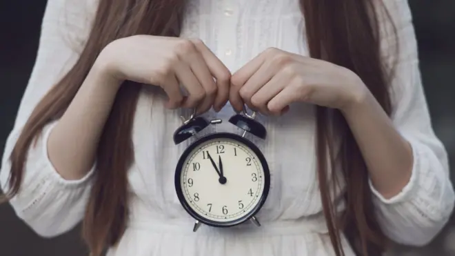 Una mujer sostiene un reloj en su vientre.