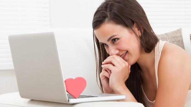 Una muchacha mira una laptop sonriente y abajo hay un corazoncito de cartón.