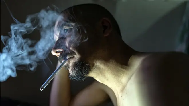 Bearded man smoking, staring vacantly into the distance