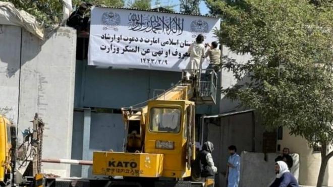 People on a mechanical crane attend to a white signboard outside a building in Kabul