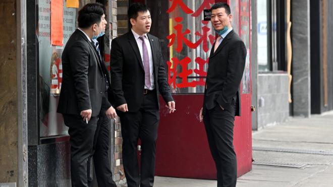 Men wearing suits are seen smoking on the sidewalk in Manhattan's Chinatown
