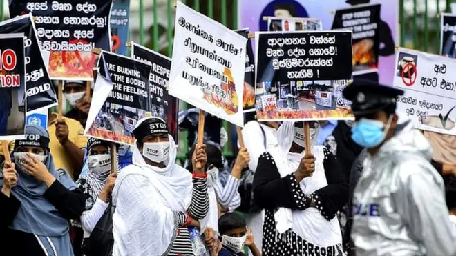 A Policeman stands guard as protesters hold placards during a demonstration against the government policy of forced cremations of Muslims who died of the Covid-19 coronavirus, outside a cemetery in Colombo on December 31, 2020