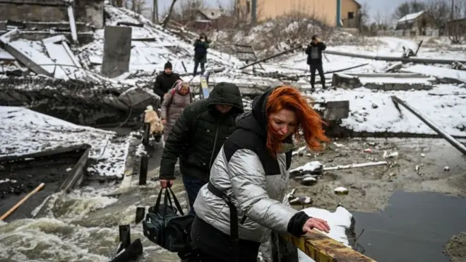 Civilians cross a river on a blown up bridge on Kyiv's northern front on March 1, 2022
