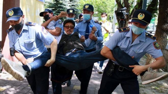 Протестующего уносят полицейские во время акции 6 июня в Алматы