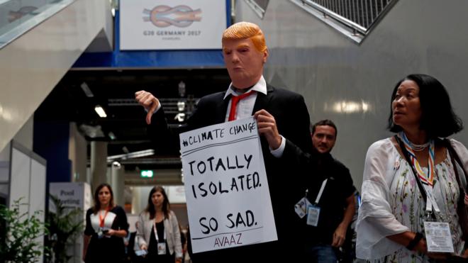 汉堡G20峰会会场内一名男子带起特朗普面具并举起调侃他因气候变化问题遭到孤立的标语牌（9/7/2017）