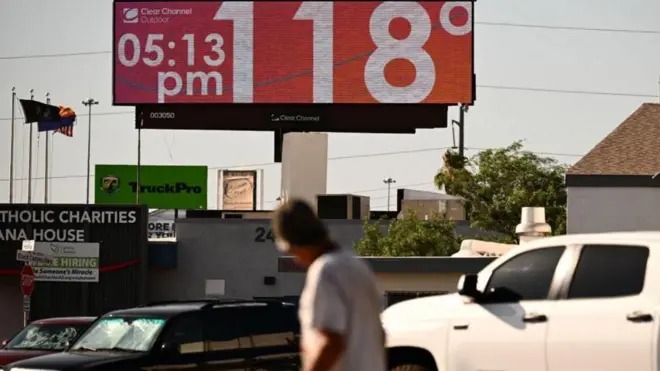 Un hombre camina por la calle y mira hacia arriba, hacia un cartel que indica 118 grados y las 17:15 h.