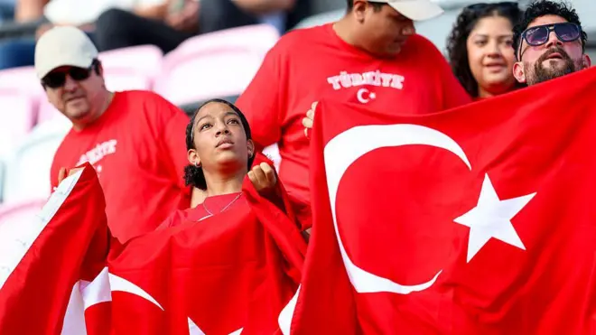 Siyah bir Türk bayraklı kadın Türkiye'nin maçında milli oyuncular desteliyor. Yanında ona bakan biri var