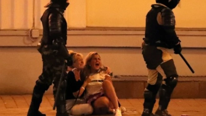 Two women on the floor, screaming, while two policemen with batons stand next to them