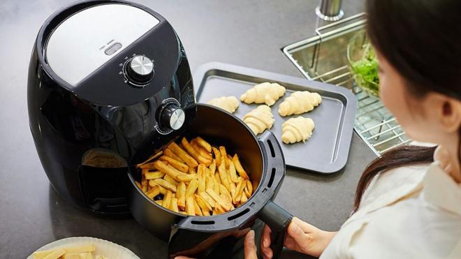 Mulher usando air fryer para fazer batata frita