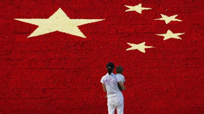 A woman holds her son as she looks at the national flag made up of 100,000 carnations at Wuling Square September 25, 2007 in Hangzhou, China.