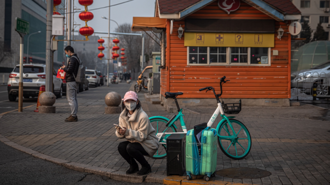 Женщина сидит у сумок на обочине дороги в Пекине