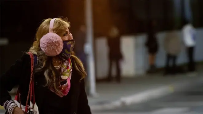 A woman wearing a protective face mask and earmuffs crosses the street during the outbreak of the coronavirus disease) in Beverly Hills, California, US, November 20, 2020