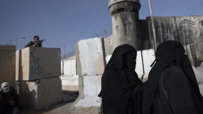 An Israeli soldier watches as Palestinians women wait to cross Qalandia checkpoint to attend the first Friday prayer service of Ramadan at the al-Aqsa Mosque in occupied East Jerusalem (16 April 2021)