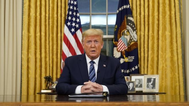 Donald Trump sentado diante de mesa na Casa Branca fazendo discurso