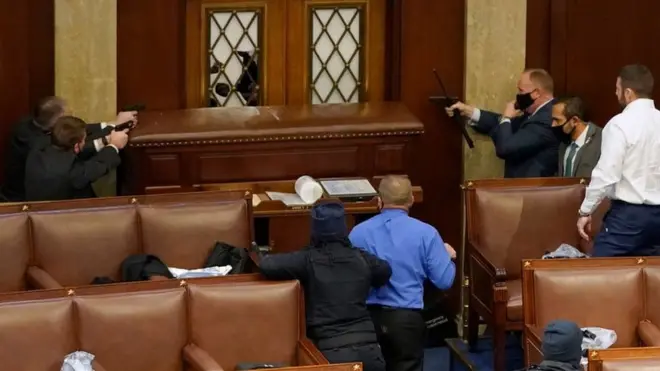 Capitol police officers point guns at a protester from inside the Senate chamber