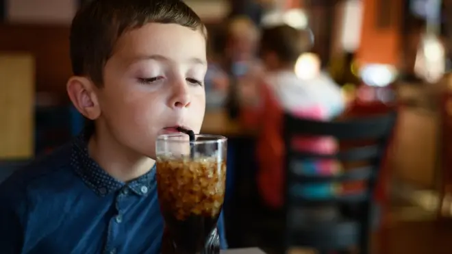 Un niño toma una bebida cola.