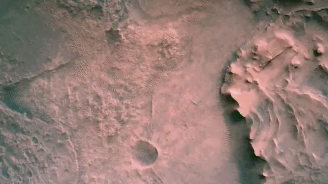 अवतरणका लागि तल झर्दै गर्दा देखिएको जेजेरो क्रेटर। यो तस्बिरको मध्य बायाँतर्फ अवतरण गरेको थियो। दायाँतर्फ भएको उठेको भाग प्राचीन समयमा बग्दै आएको नदीले काटेको भूभाग मानिन्छ। यो ठाउँबाट रोभरले माटो र चट्टान निकालेर ट्यूबहरूमा भर्नेछ जुन भविष्यमा पृथ्वीमा ल्याउने योजना छ।