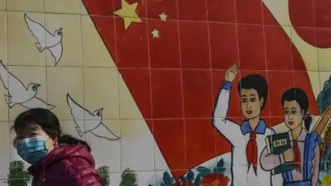 A woman wears a mask as she passes a propaganda mural in Beijing, China. Photo: 8 February 2020