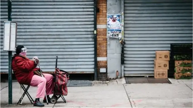 A woman wearing a scarf and goggles wait for a bus to arrive in a bus stop in Brooklyn