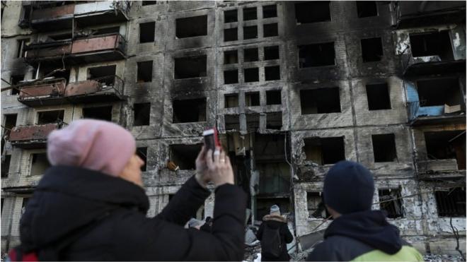 A woman takes photos of a building damaged by shelling in Kyiv