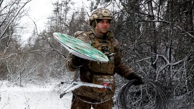A Ukrainian serviceman walks with a disconnected Starlink terminal
