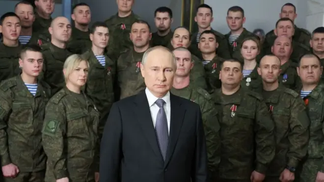 Le président Vladimir Poutine prononce son discours du Nouvel An entouré de personnes en uniforme.