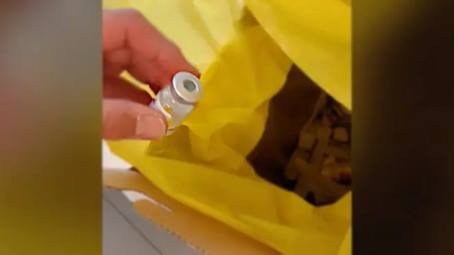 มือคนจับขวดวัคซีนเตรียมทิ้งลงถังขยะ