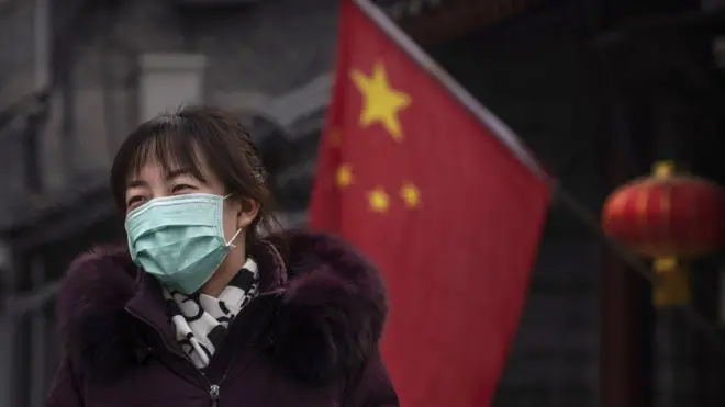 A Chinese woman wears a protective mask as she walks by a flag and lantern placed for the Chinese New Year holiday on January 26, 2020 in Beijing