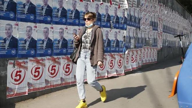 Женщина идет вдоль стены с рекламой кандидатов