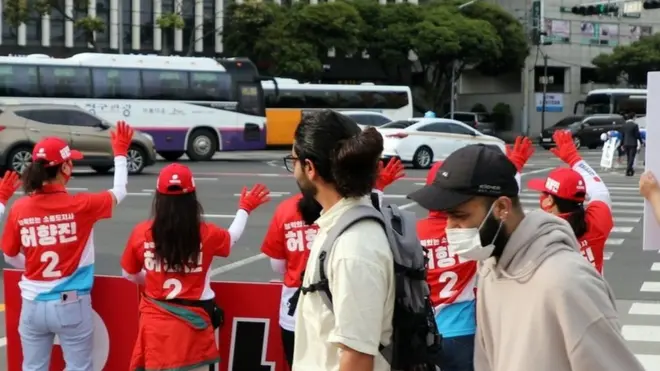 지난 6월 1일 지방선거 공식 선거운동 첫날인 5월 19일 오전 제주시 신광로터리에서 외국인들이 국민의힘 허향진 후보 선거운동원들이 거리인사하는 모습을 보고 있다