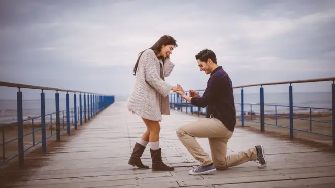 رجل يجثو على ركبته ويضع خاتماً في يد فتاة