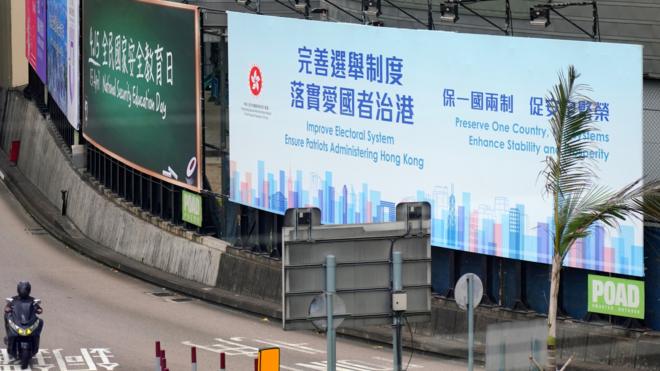 A motorcyclist rides past a billboard reading 'Improve Electoral System, Ensure Administering Hong Kong, Preserve One Country, Two System, Enhance Stability and Prosperity' in the street on March 31, 2021 in Hong Kong, China