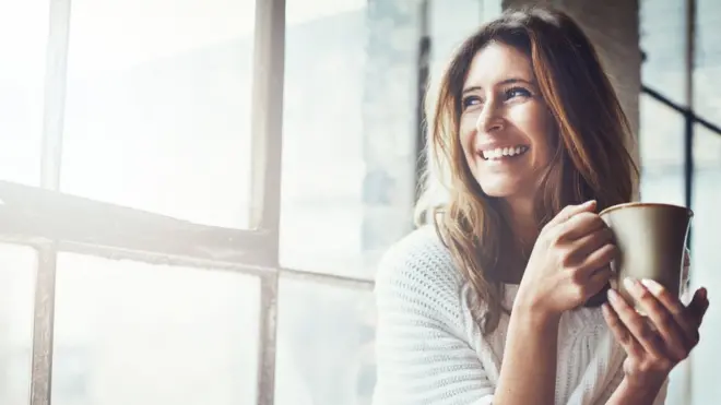 Chica con una taza al lado de una ventana.